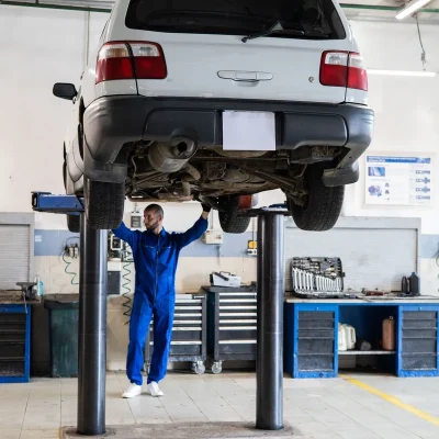 Mecânico inspecionando carro no lift comunica suporte automotivo real, safety e oficina sem parecer anúncio genérico.